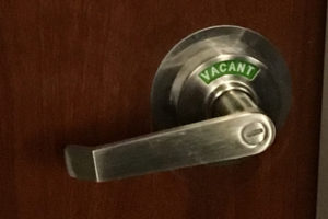 A lever-style doorknob with a sliding section that displays "Vacant" in white letters on a green background or "Occupied" in white letters on a red background depending on the position of the lock.