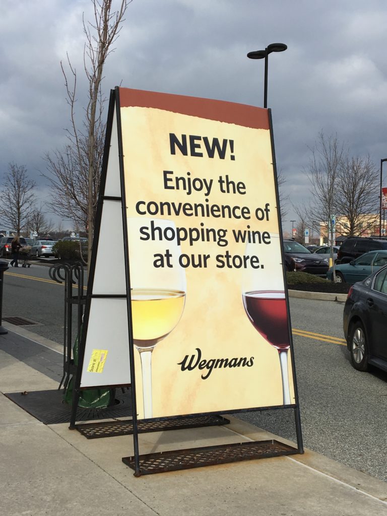 A-frame sign at a Wegman's supermarket that reads" New! Enjoy the convenience of shopping wine at our store".